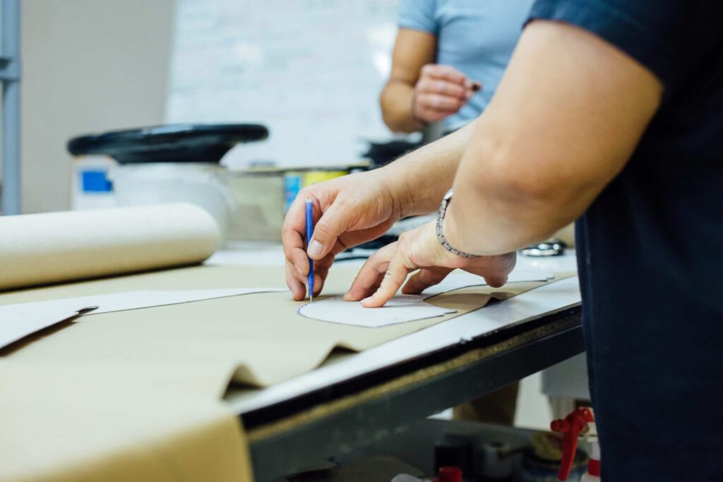 hands of a craft person preparing the design of the leather on the table cutting mat for upholstering the interior car components in a upholstery factory
